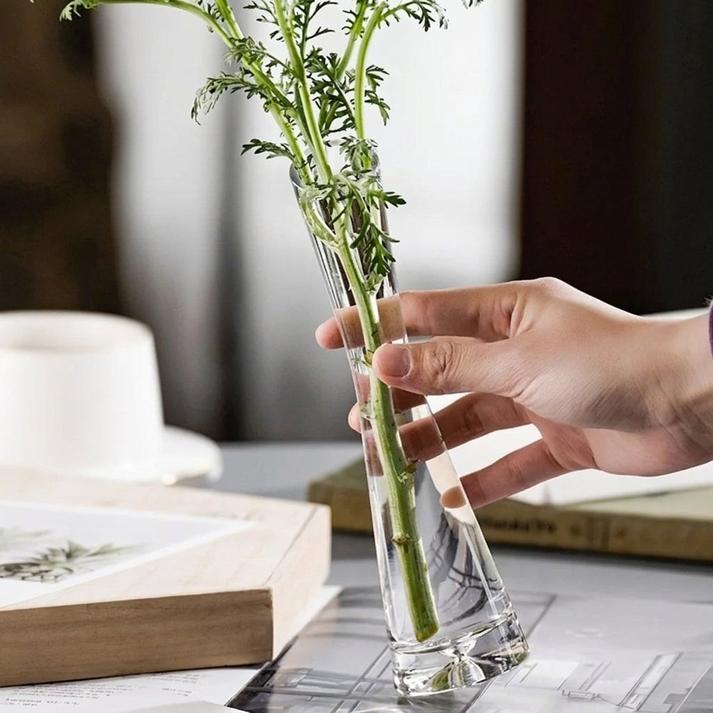 Vase soliflore en verre à bouche inclinée tenu en main avec du feuillage