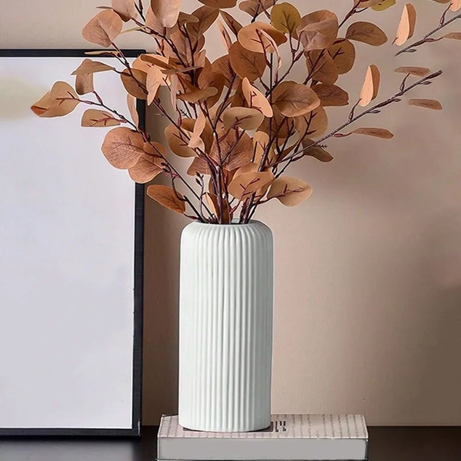 Vase blanc à rainures garni de feuillage séché posé sur des livres
