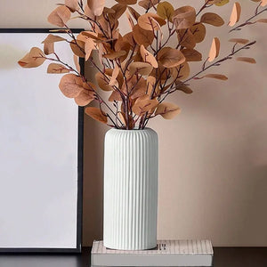 Vase blanc à rainures garni de feuillage séché posé sur des livres