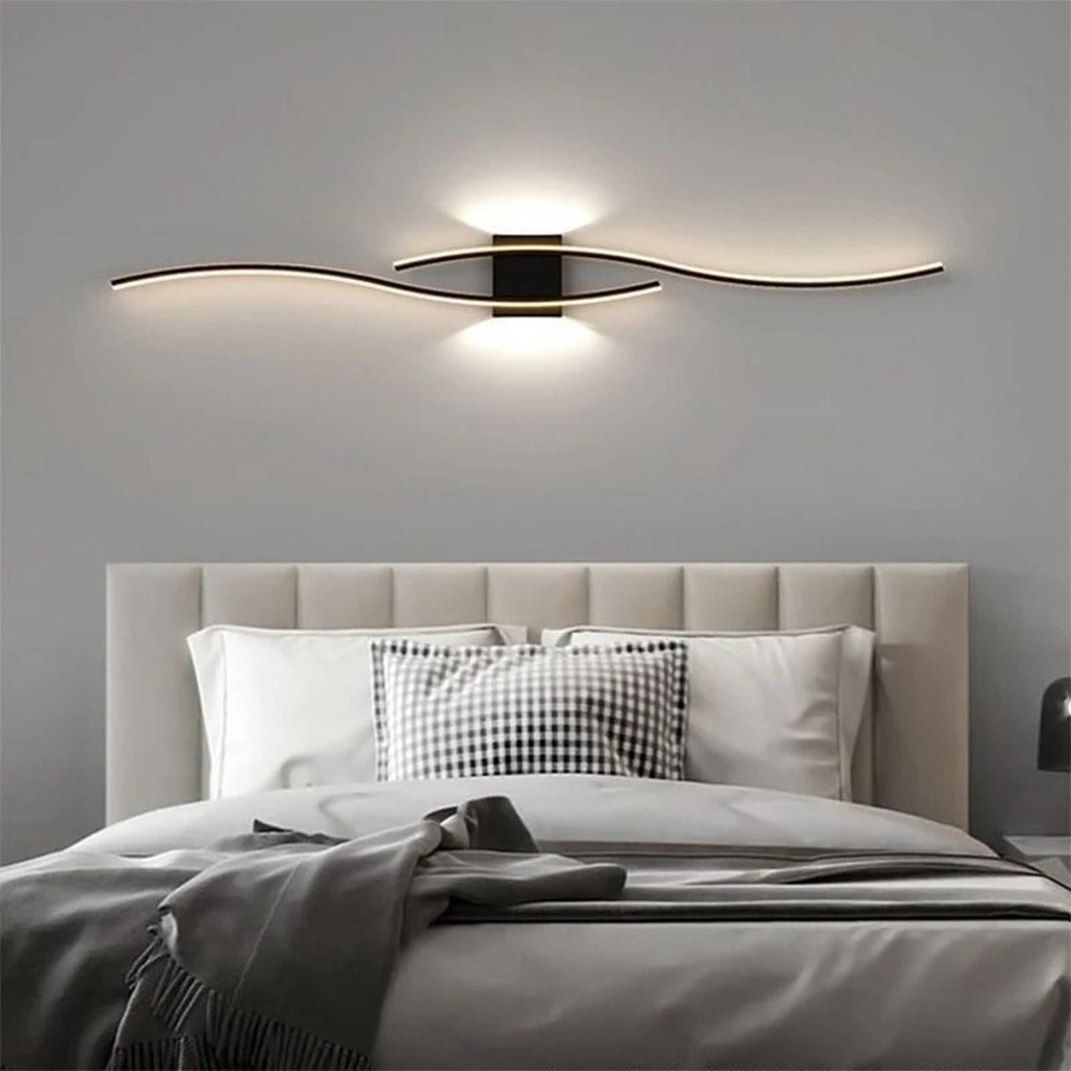 Applique murale noire double courbe LED allumée au dessus d'un lit dans une chambre chaleureuse