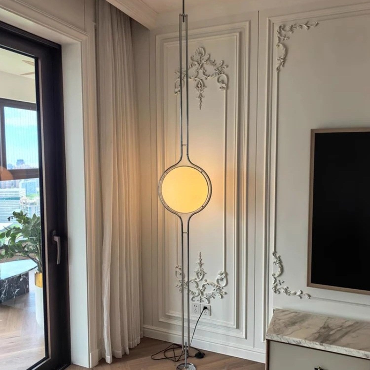 Lampadaire boule chrome du sol au plafond allumé contre un mur à moulures