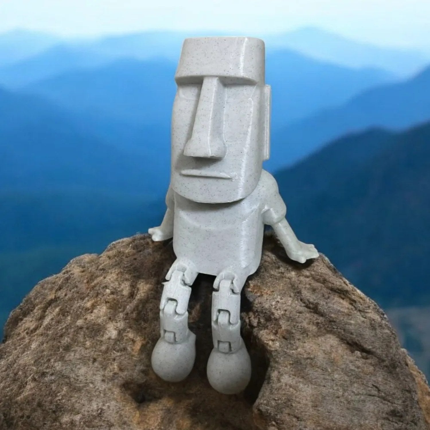 Figurine Moai grise posée sur un rocher avec un paysage de montagnes en arrière-plan