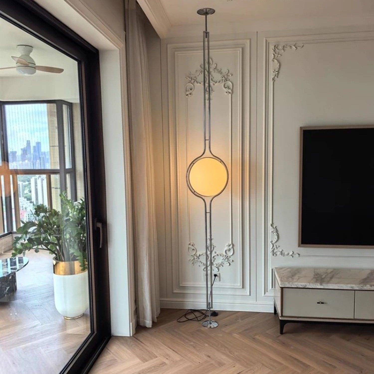 Lampadaire boule chrome installé du sol au plafond dans un salon lumineux