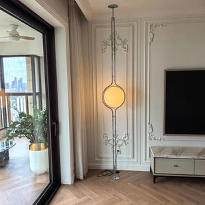 Lampadaire boule chrome installé du sol au plafond dans un salon lumineux