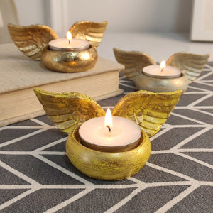 Bougeoir ailes d'ange doré en résine avec bougie allumée sur nappe géométrique