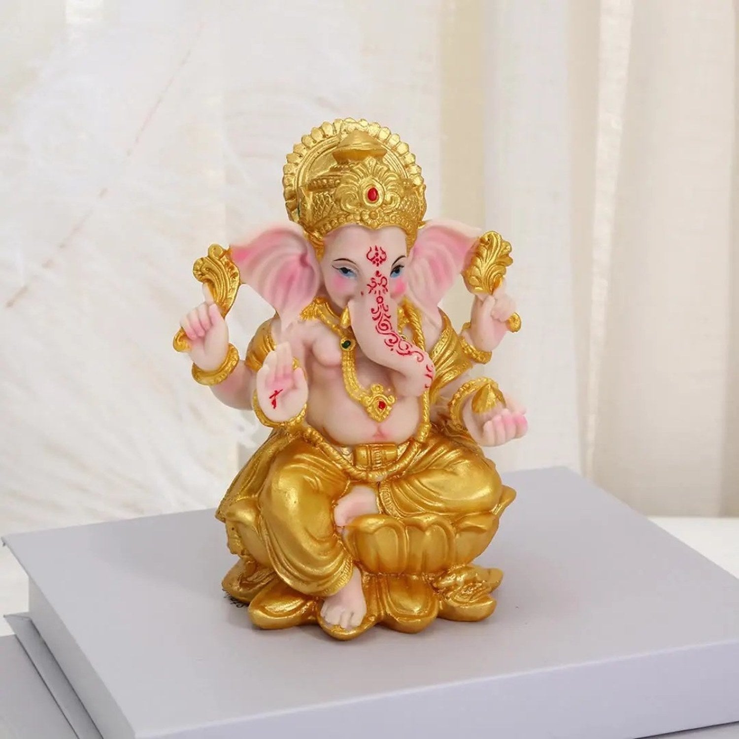Vue de face de la statue de Ganesha en résine dorée sur socle gris fond marbre