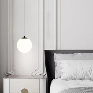 Suspension boule en verre opalin noire près d'une table de chevet blanche