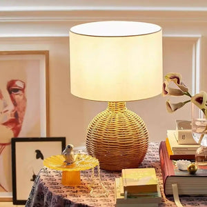 Lampe à poser rotin forme colonne allumée sur une table avec fleurs et livres