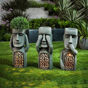 Trois statues Moai dans un jardin avec panneaux ajourés illuminés à la nuit tombée