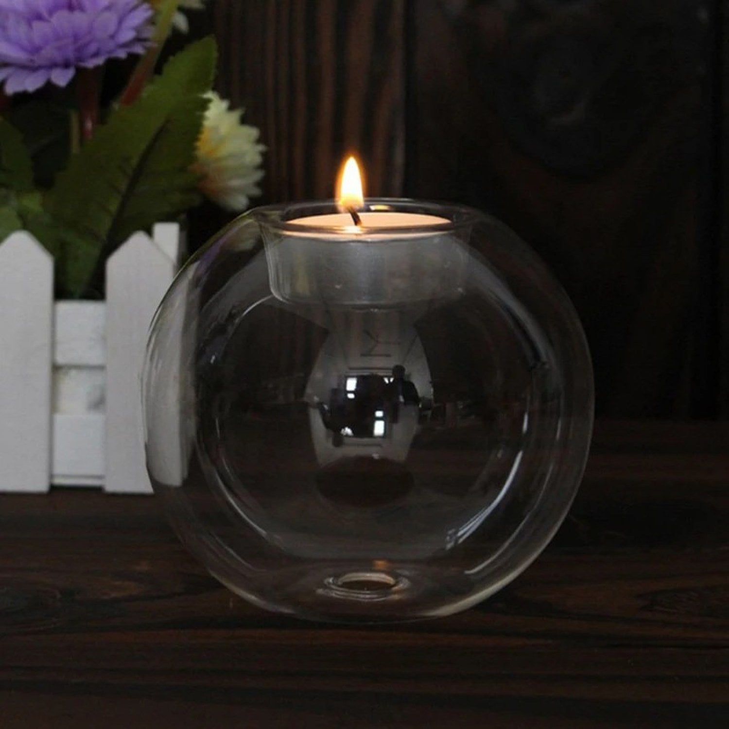 Bougeoir boule en verre transparent allumé près d'un bouquet de fleurs