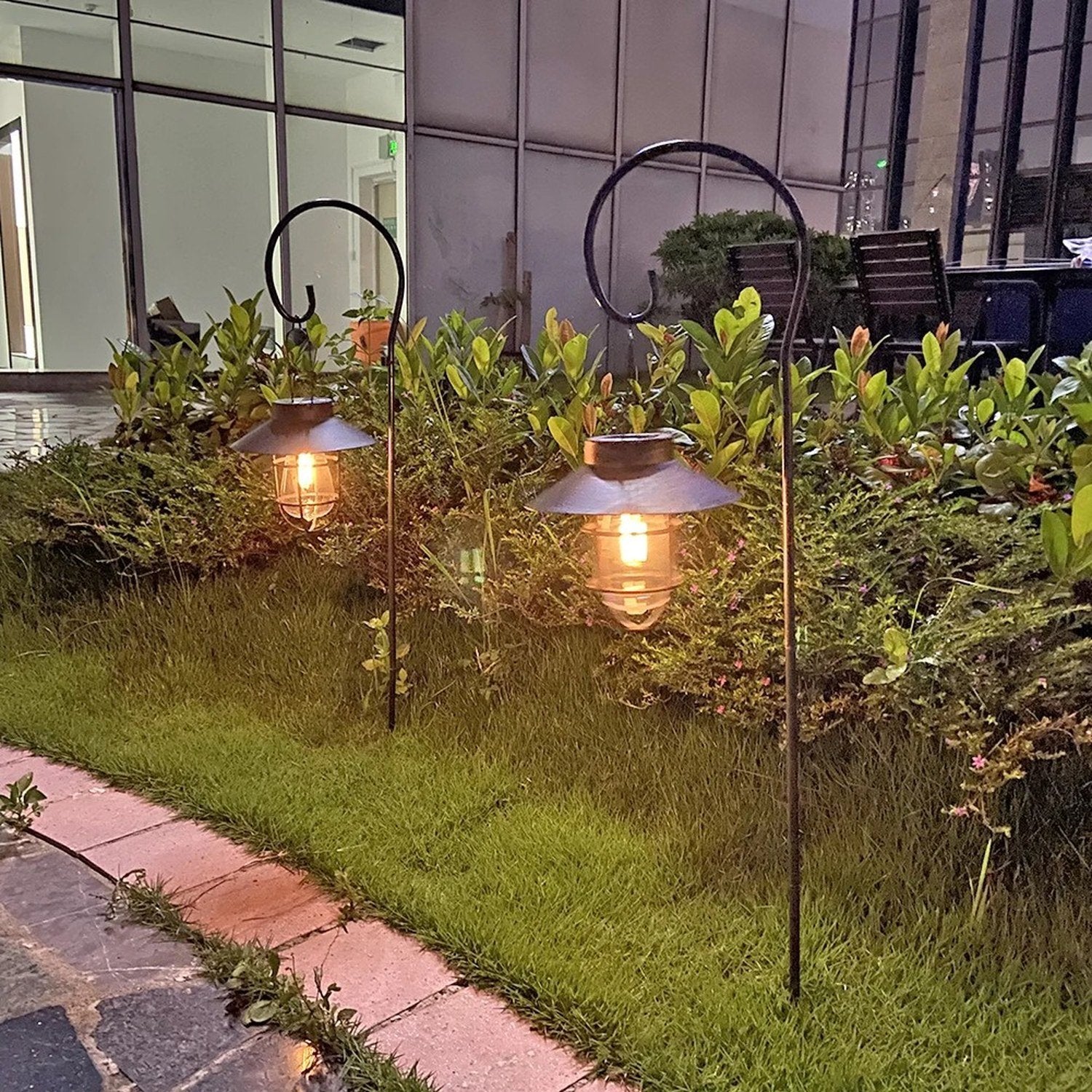 Deux lanternes solaires allumées sur des piquets dans un massif de jardin au crépuscule
