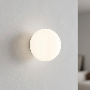 Applique murale boule en verre dépoli allumée en lumière blanche sur un mur clair