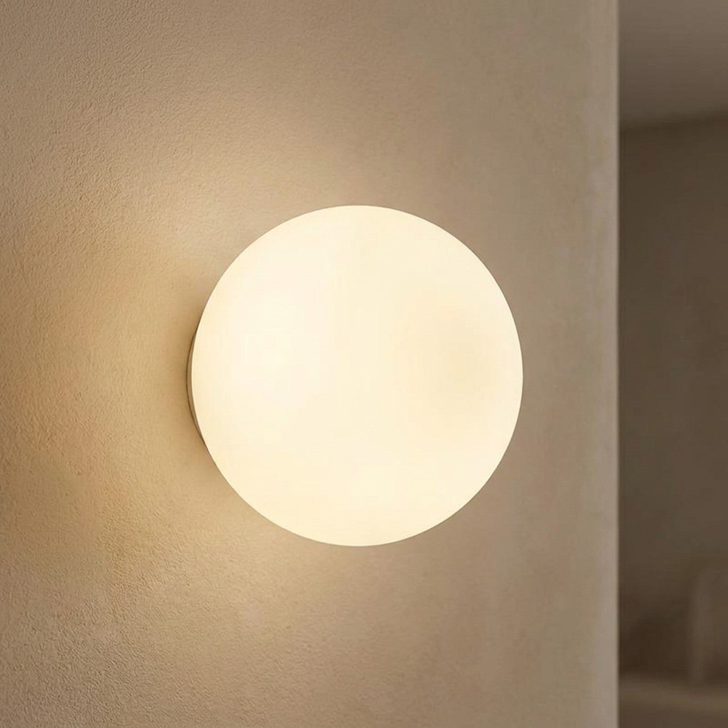 Applique murale boule en verre dépoli blanc allumée diffusant une lumière chaude sur un mur clair