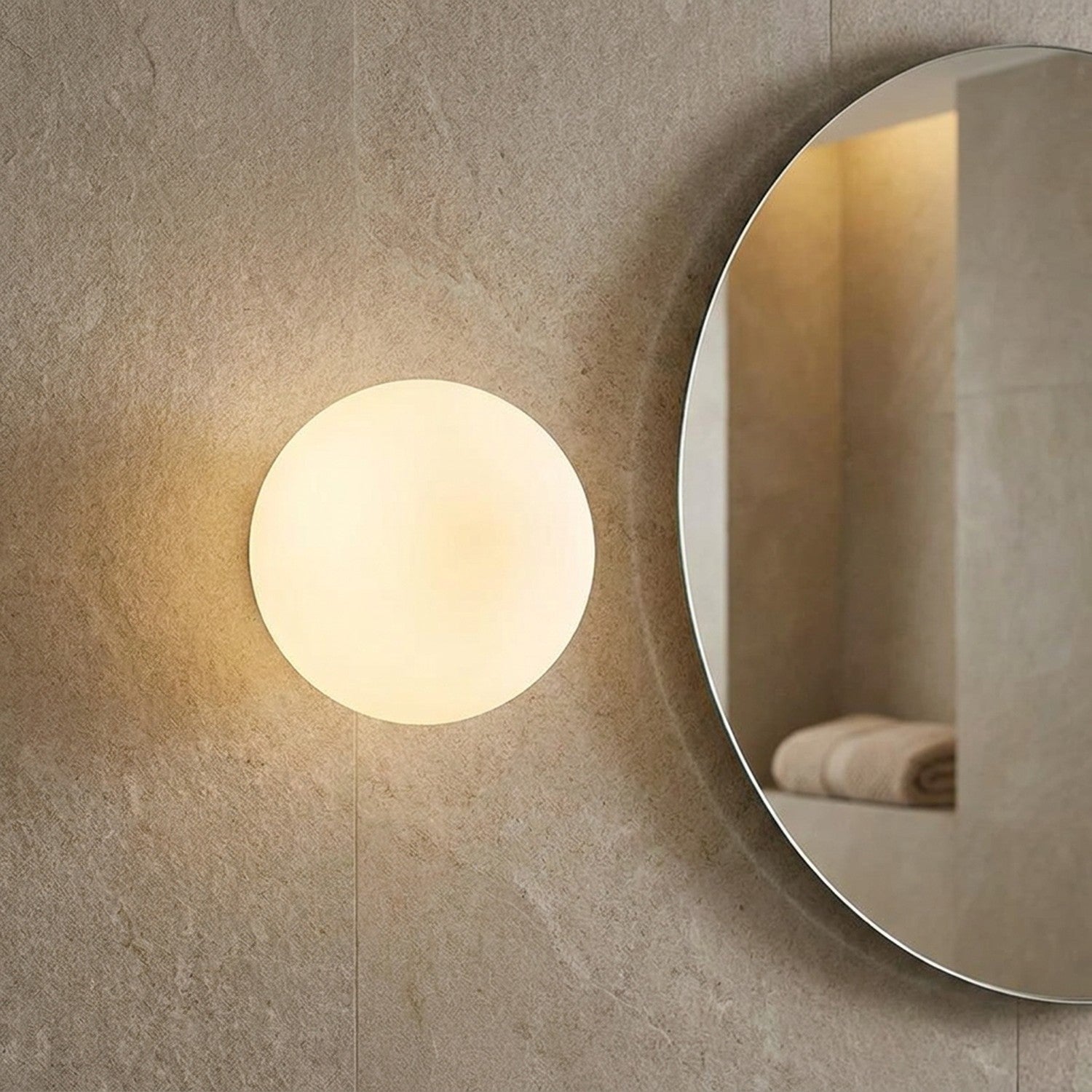 Applique murale boule en verre dépoli allumée à côté d'un miroir rond de salle de bain