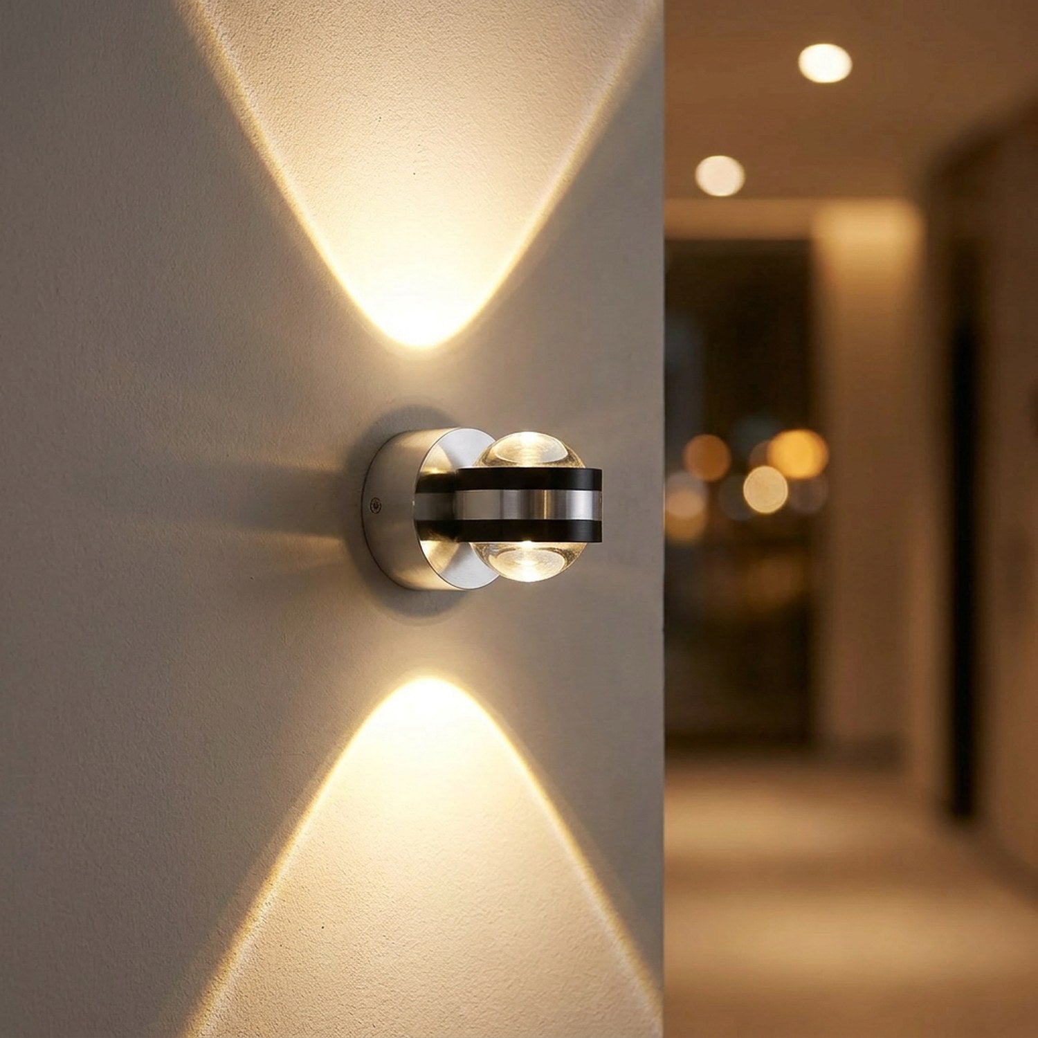 Applique murale LED ronde argentée projetant un double faisceau de lumière chaude sur un mur