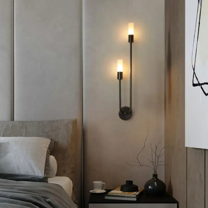 Applique murale noire installée au-dessus d'une table de chevet avec vase et livres