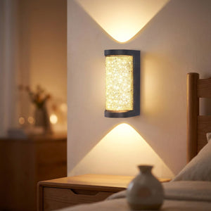 Applique murale grise avec diffuseur effet cristal illuminé projetant une lumière chaude sur un mur de chambre