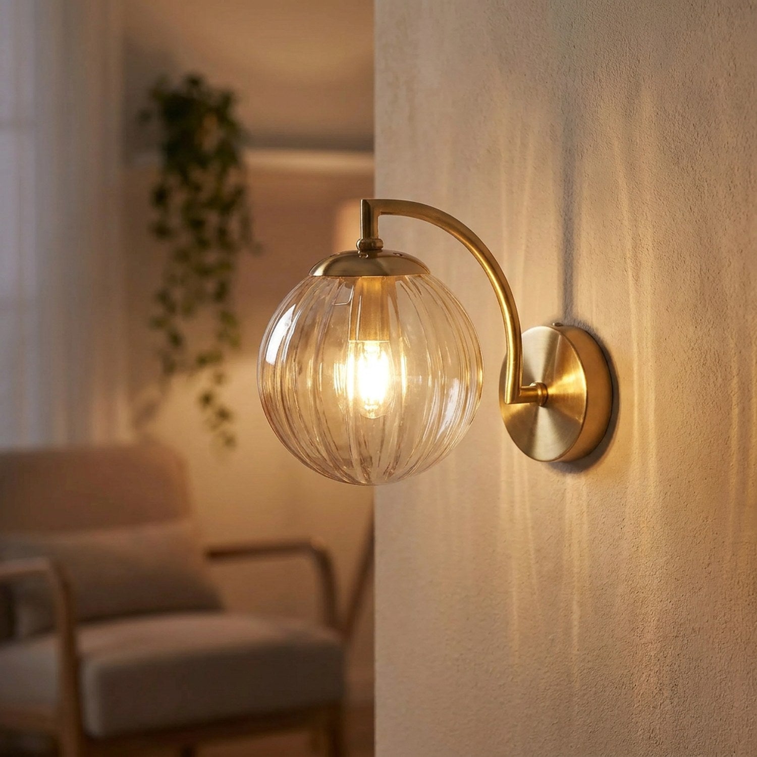Applique murale LED avec globe en verre ambré et bras en laiton doré allumée sur un mur clair