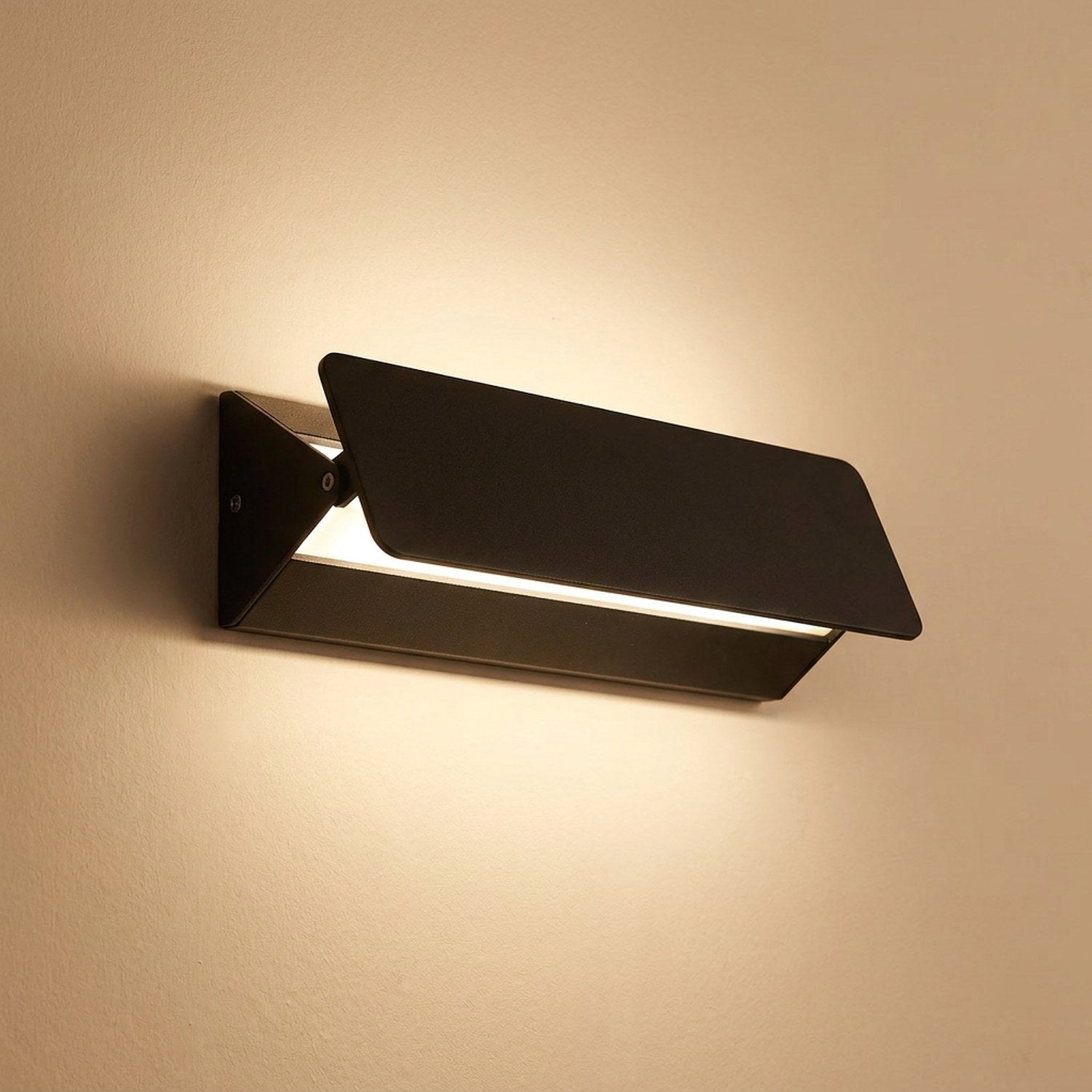 Applique murale LED noire en aluminium diffusant une lumière chaude sur un mur clair
