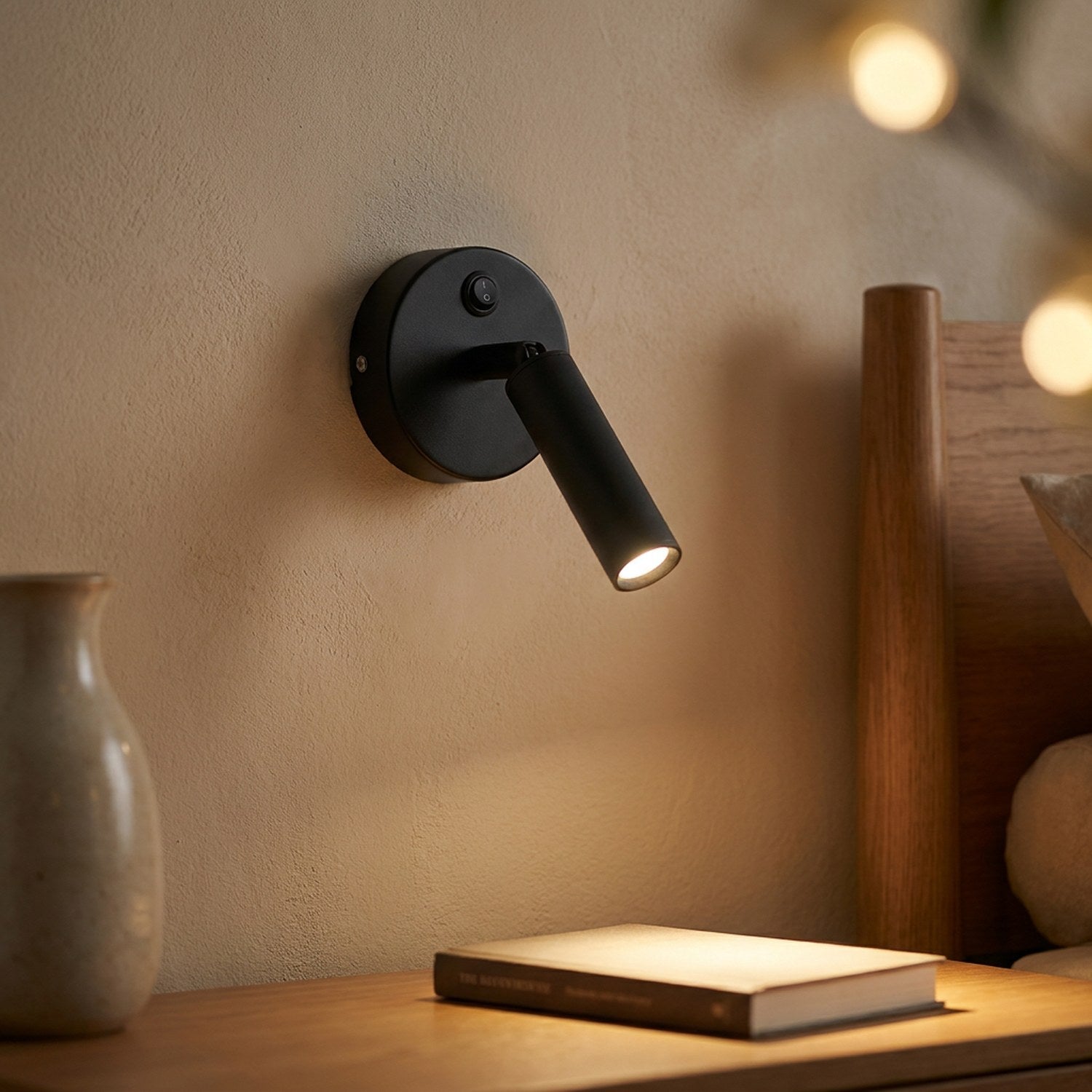 Applique murale noire au bras pliant orientable avec spot LED allumé dans une chambre chaleureuse