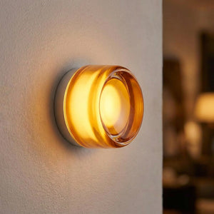 Applique murale ronde en verre ambré diffusant une lumière chaude sur un mur clair