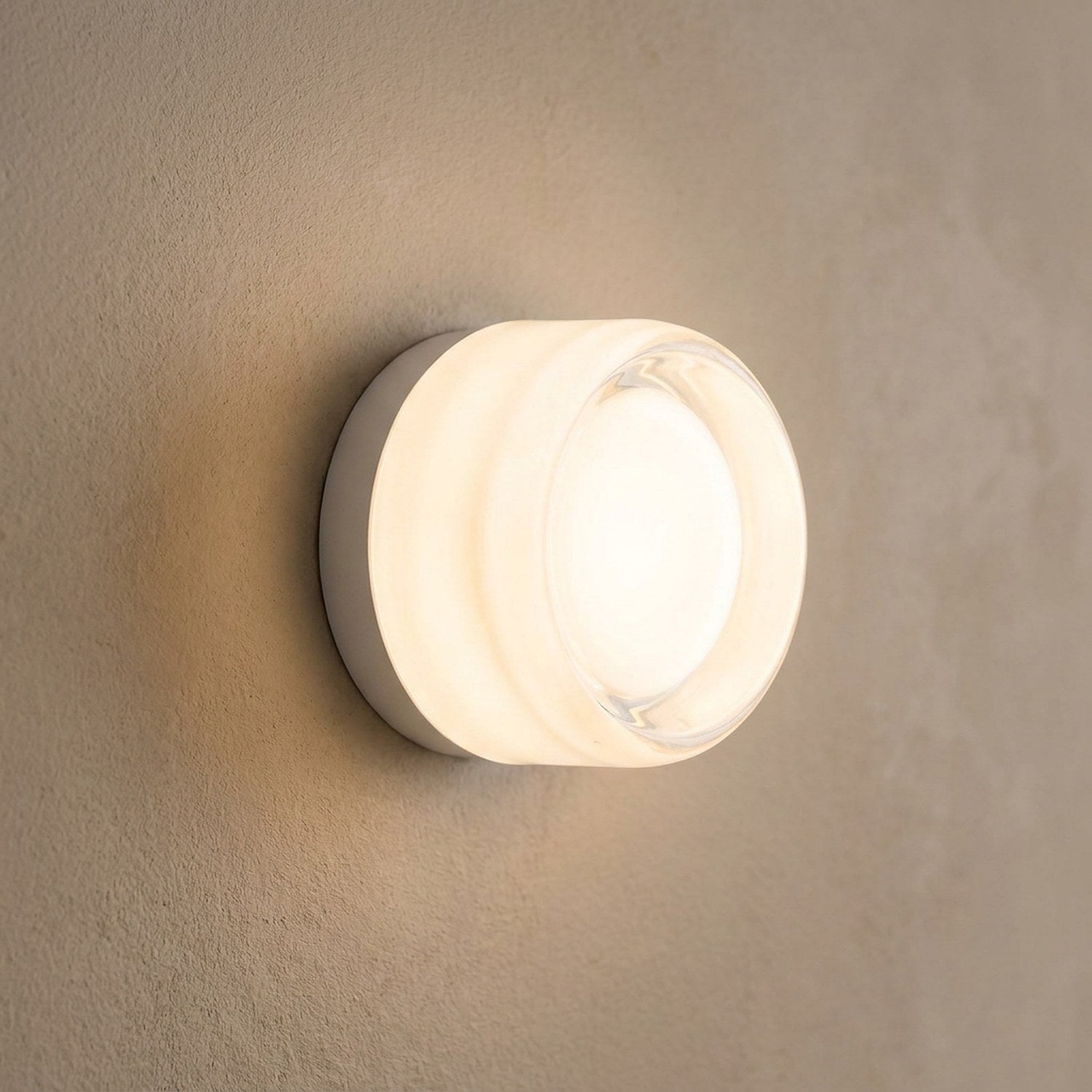 Applique murale ronde en verre blanc diffusant une lumière chaude sur un mur clair