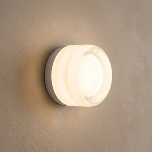 Applique murale ronde en verre blanc diffusant une lumière chaude sur un mur clair