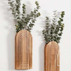 Deux vases muraux en bois arqué garnis d eucalyptus accrochés à un mur blanc