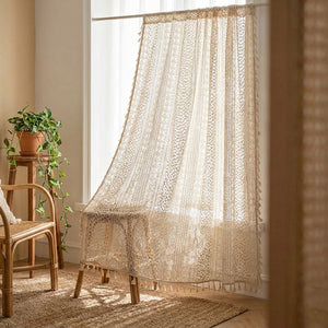 Rideau voilage boho en dentelle au crochet beige à pompons suspendu à une fenêtre lumineuse