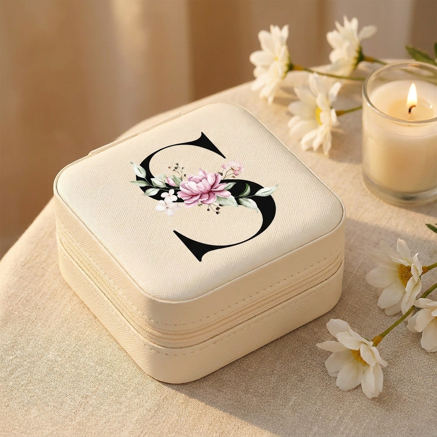 Boîte à bijoux de voyage sur tissu lin beige avec fleurs blanches et bougie ambiance dorée