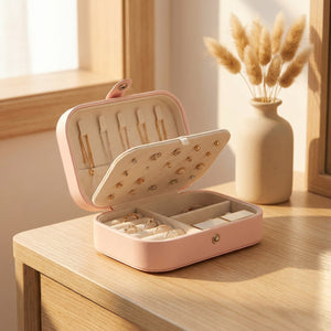Boite à bijoux de voyage rose en simili cuir posée ouverte sur une coiffeuse en bois avec bougie et herbes de pampa