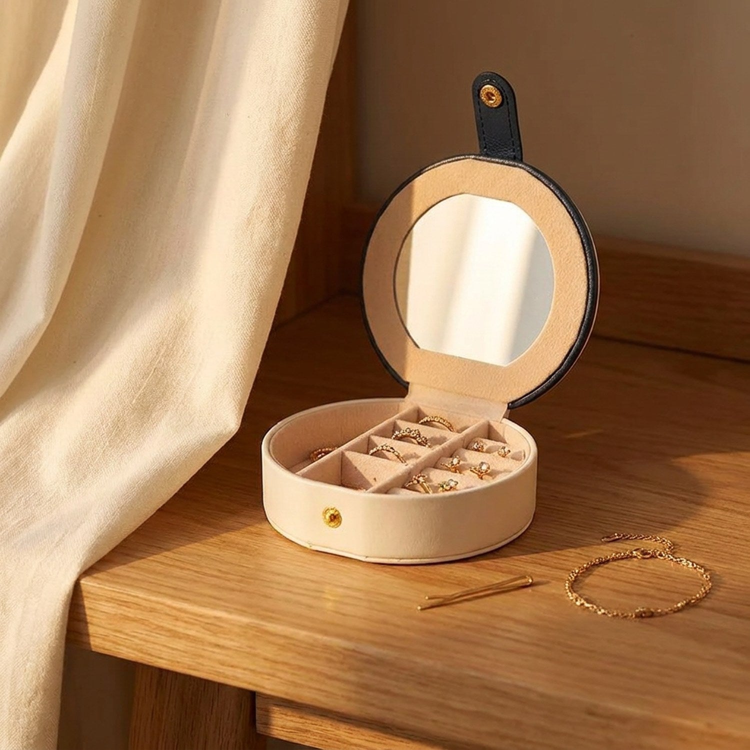 Boîte à bijoux ronde blanche ouverte sur une table en bois avec bagues et boucles d'oreilles