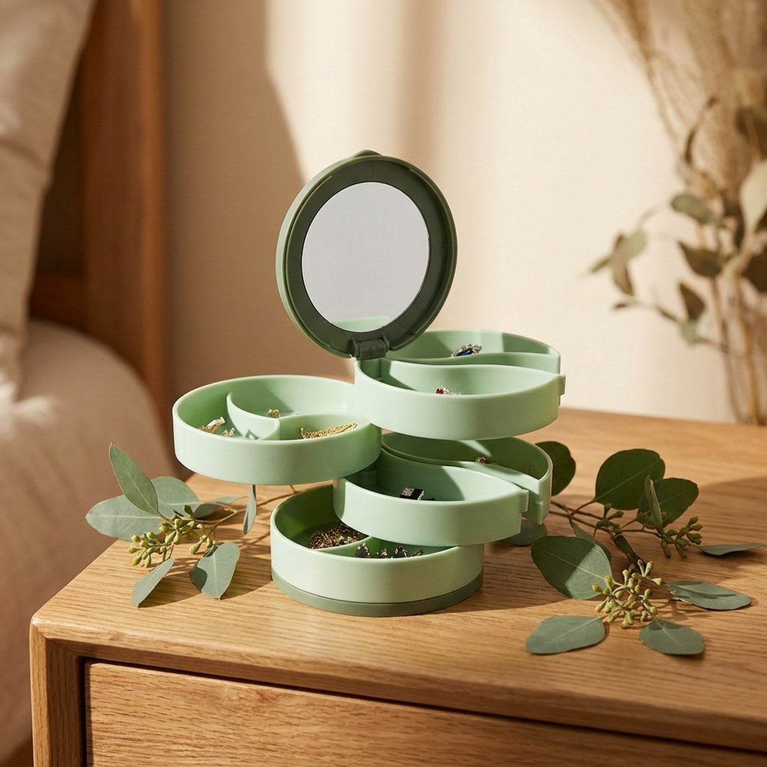 Boîte à bijoux rotative verte ouverte sur table de nuit avec eucalyptus