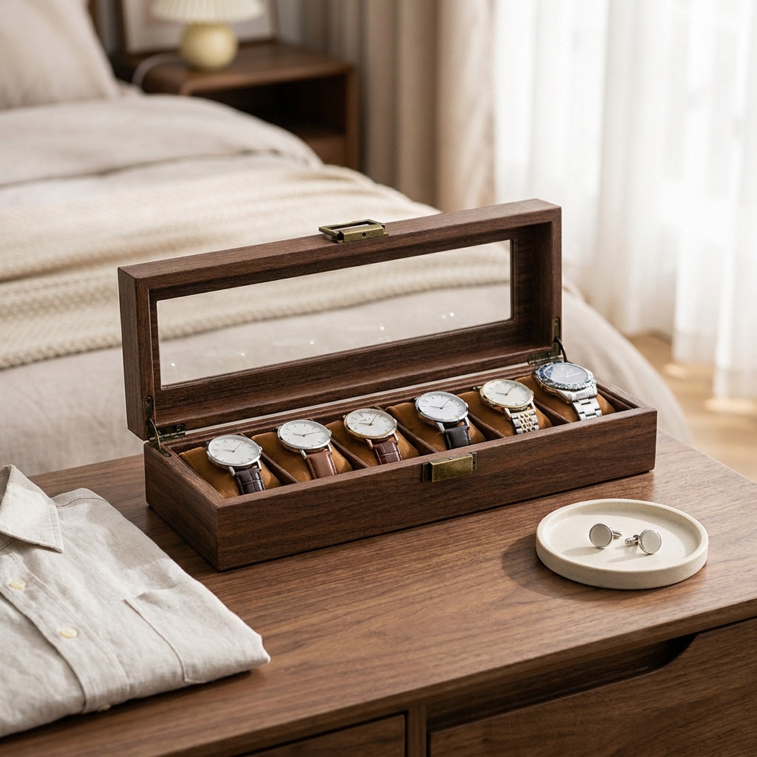 Boîte à montres en bois ouverte sur une table de chevet avec une chemise pliée et des boutons de manchette