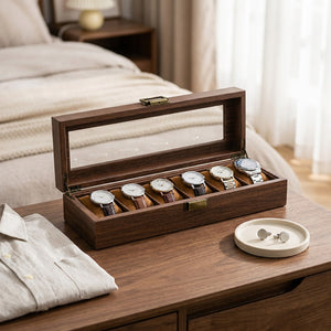 Boîte à montres en bois ouverte sur une table de chevet avec une chemise pliée et des boutons de manchette