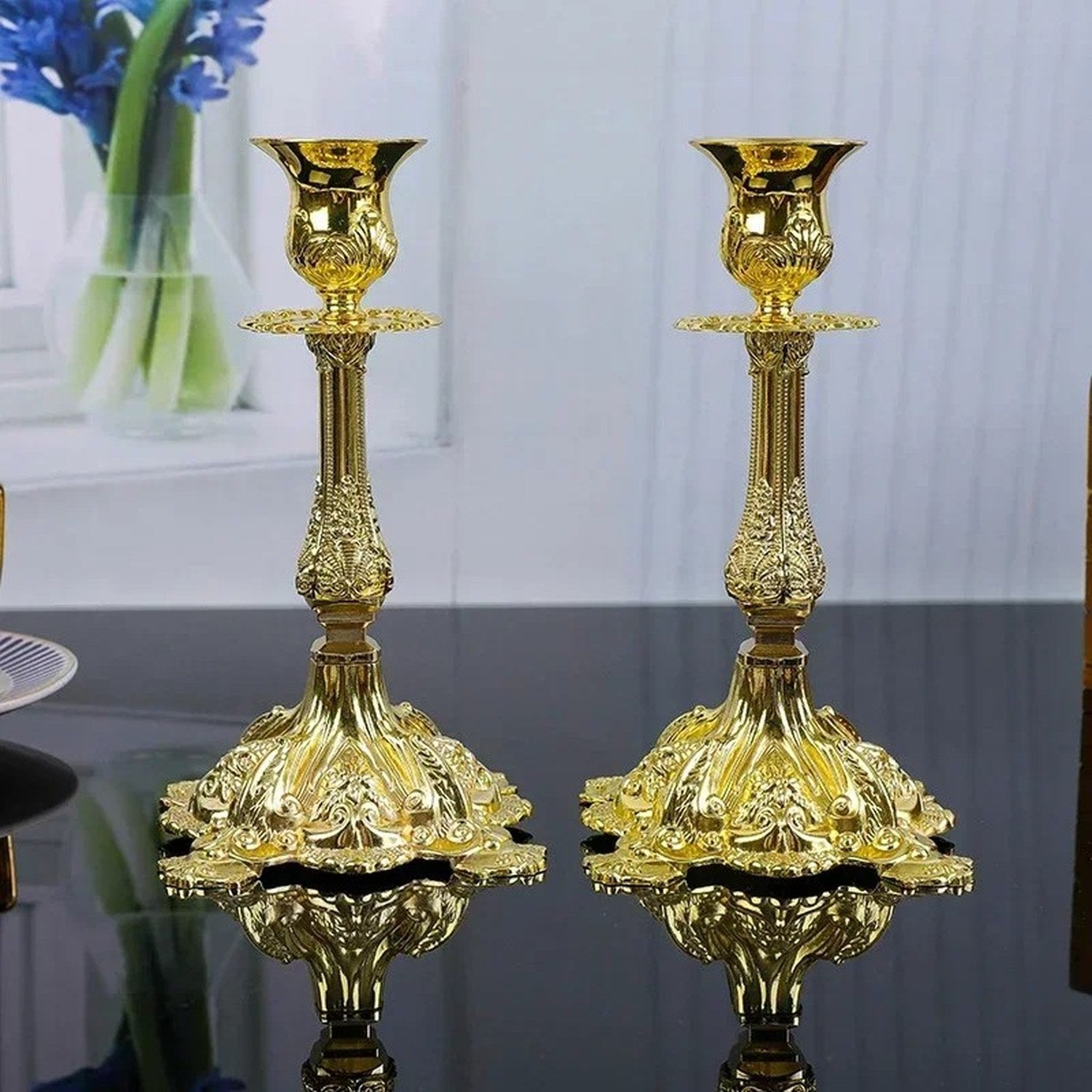 Vue de face de deux bougeoirs en métal doré baroque sur surface réfléchissante