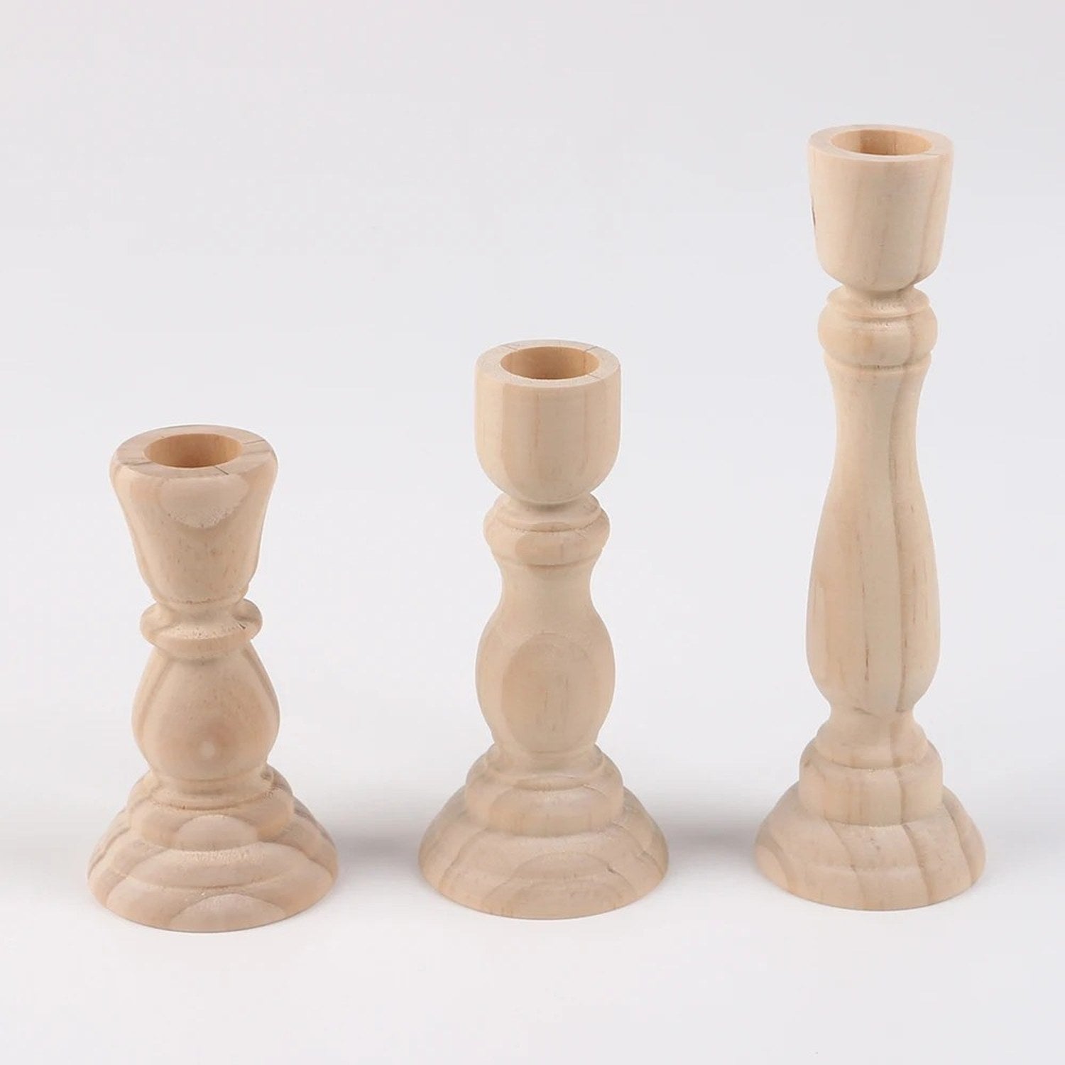 Trois bougeoirs en bois brut tourné de tailles croissantes sur fond clair