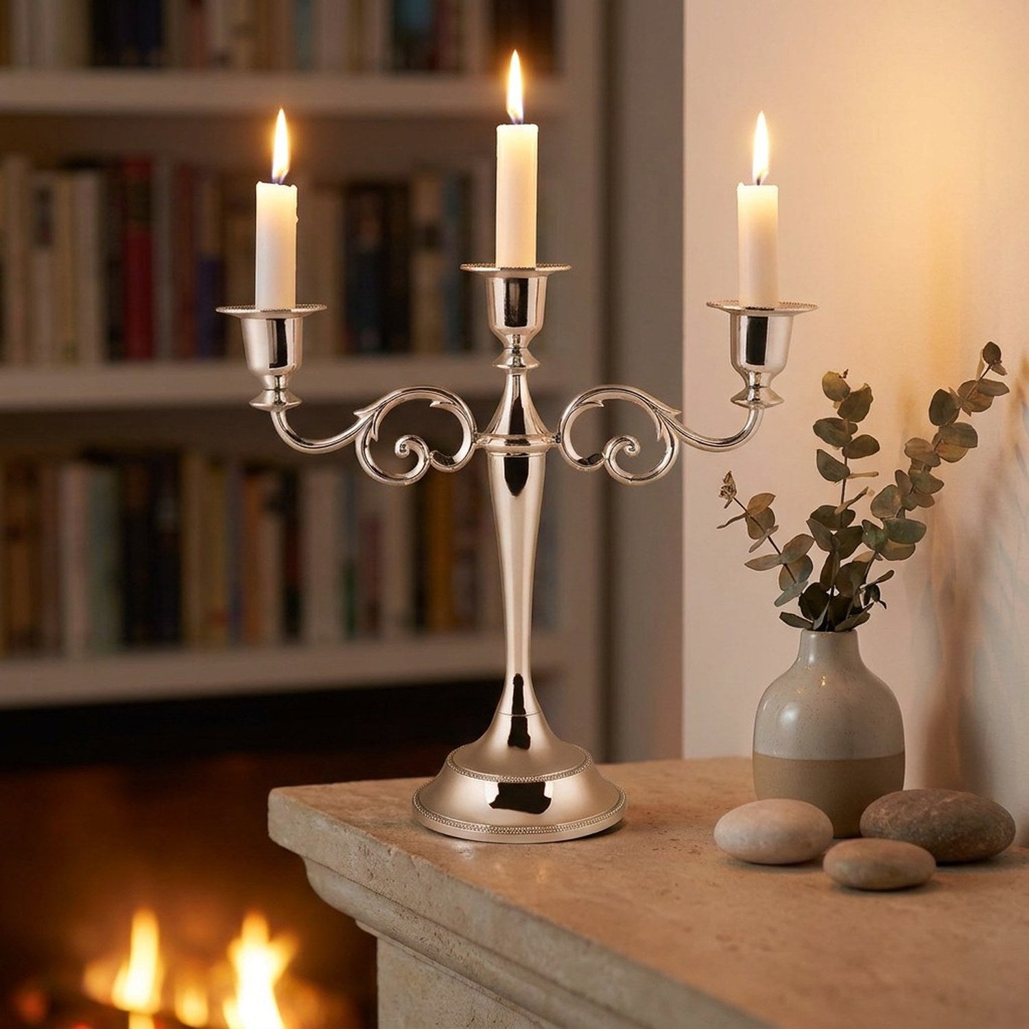 Bougeoir chandelier argenté 3 branches posé sur une cheminée avec bougie allumées