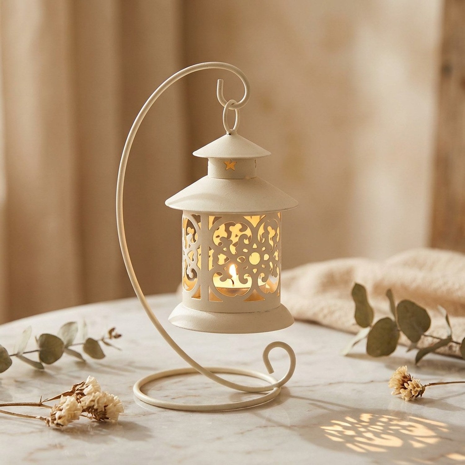 Bougeoir lanterne en fer forgé ajouré style vintage avec bougie allumée posé sur une table décorée