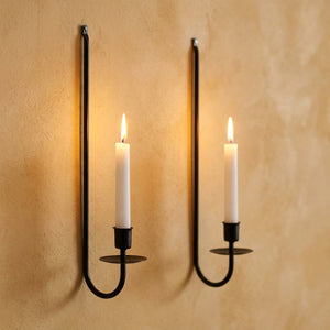 Lot de 2 bougeoirs muraux en fer forgé noir sur mur ocre avec bougies allumées