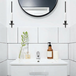 Deux bougeoirs muraux fer forgé flanquant un miroir rond dans salle de bain