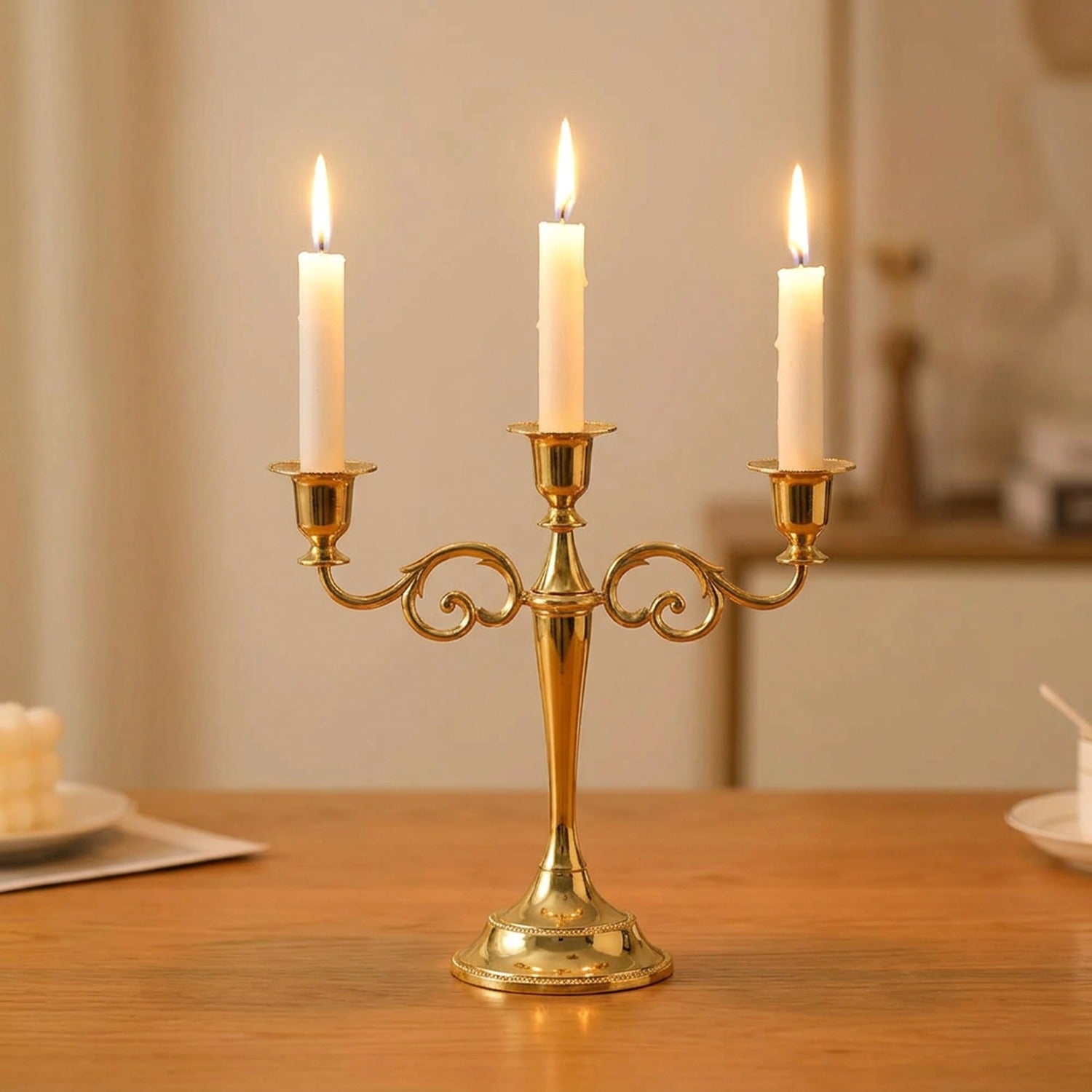 Bougeoir métal doré à 3 bras style baroque avec bougies allumées sur table en bois