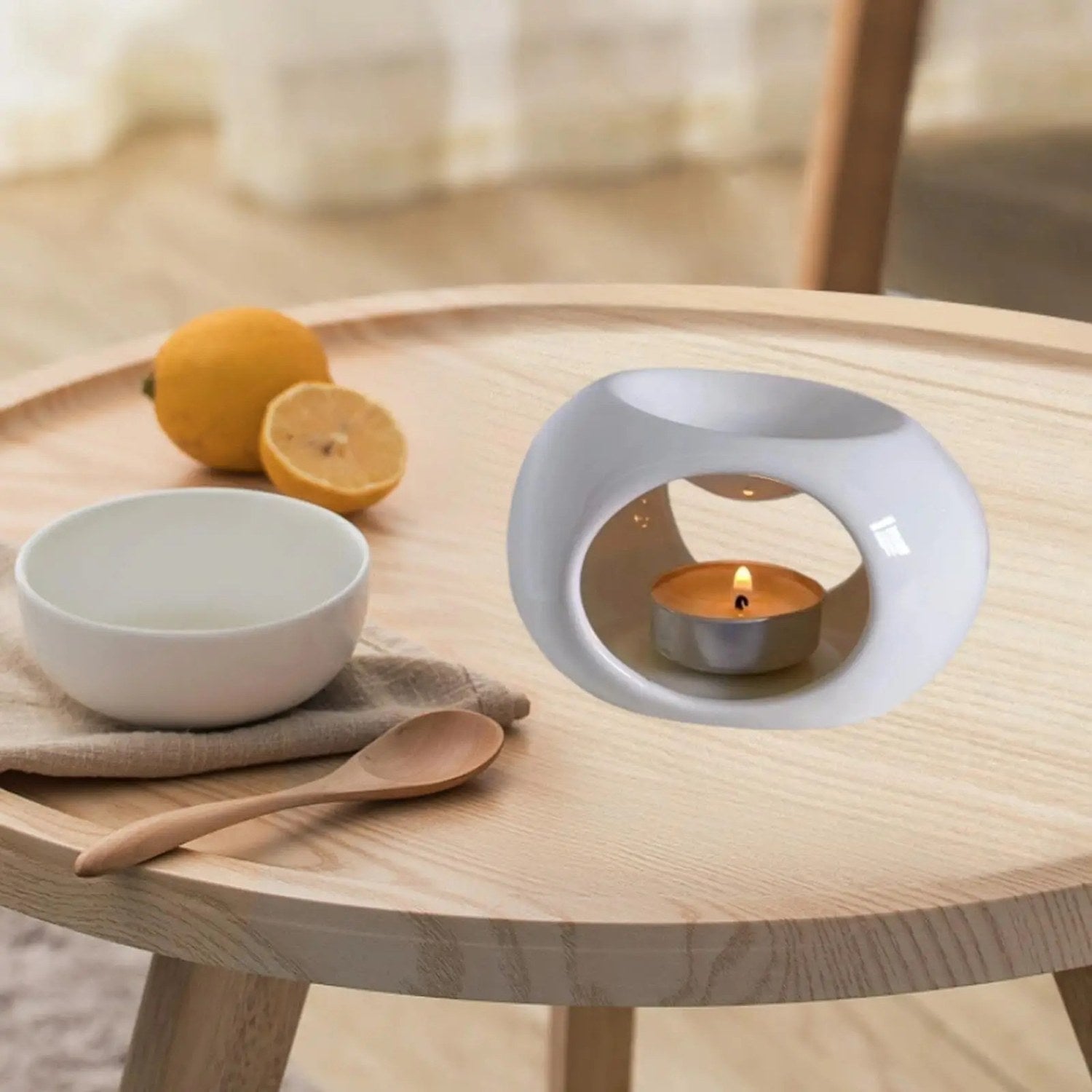Brûle-parfum céramique blanc sur table en bois avec citrons et bougie allumée