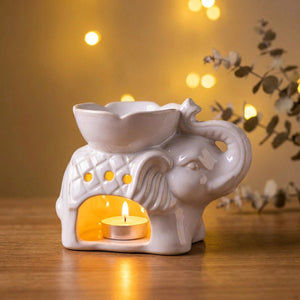 Brûle-parfum céramique blanc en forme d'éléphant avec une bougie chauffe-plat allumée sur une table en bois au coucher du soleil