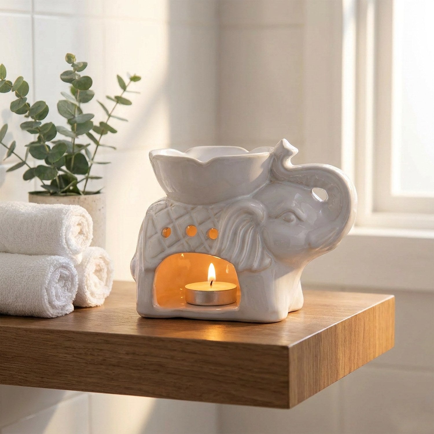 Brûle-parfum éléphant allumé posé sur une étagère de salle de bain avec serviettes roulées et plante verte