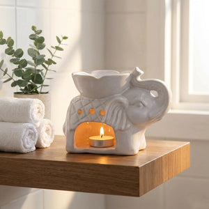 Brûle-parfum éléphant allumé posé sur une étagère de salle de bain avec serviettes roulées et plante verte