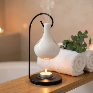 Brûle-parfum en céramique blanche suspendu avec bougie allumée sur une étagère de salle de bain