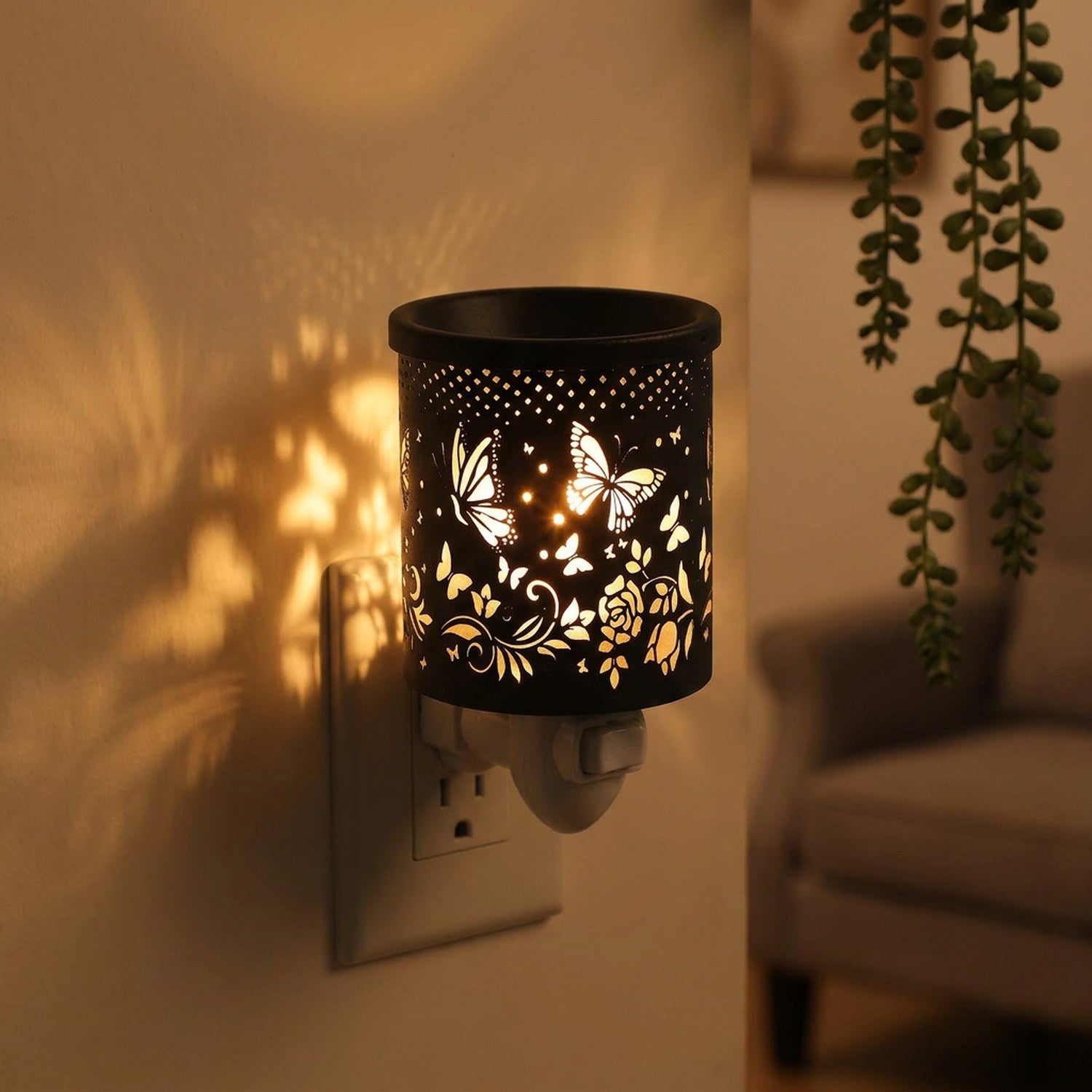 Chauffe-cire électrique en métal noir ajouré motif papillons allumé et branché sur une prise murale