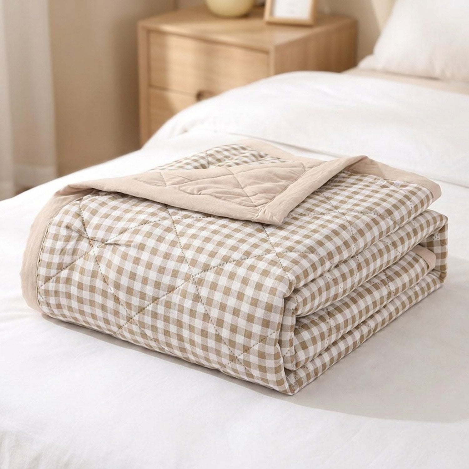 Couette d'été matelassée à petits carreaux vichy beige pliée sur un lit