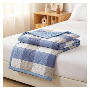Couette d'été matelassée à carreaux bleus et gris pliée sur un lit dans une chambre lumineuse